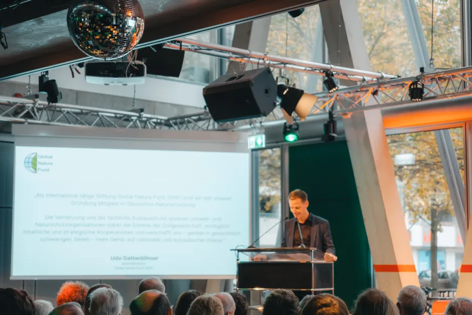 Kai Niebert am Podium, im Hintergrund Leinwand mit Glückwunschzitaten